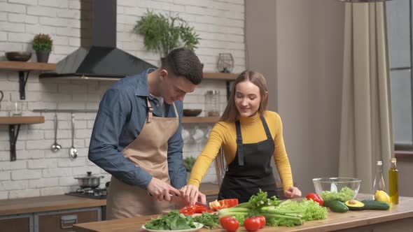 Happy couple enjoying cooking time together at home. Side view of young man cutting vegetables 