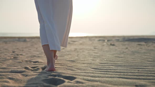 Barefoot woman in a white dress walking along the seashore