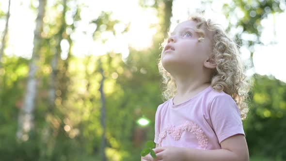 A little curly-haired girl looks into the sky on a bright sunny day