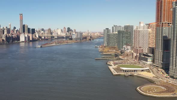 A high angle view looking north over the East River on a sunny day. The drone camera truck right and