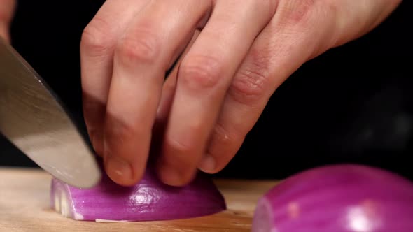 Hands is Cutting a Red Onion with a Knife on Wooden Board Closeup