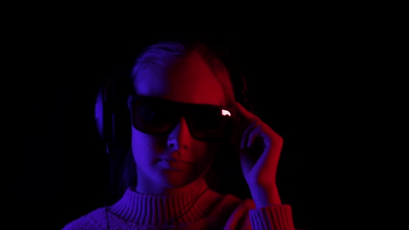Happy Girl Listening Music in Headphones and Black Sunglasses in Dark Studio with Red and Blue