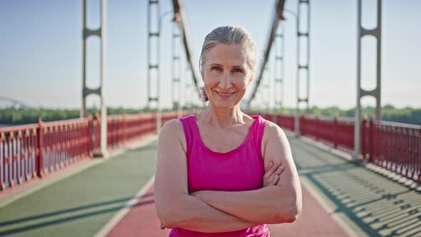 Cheerful Elderly Woman Crosses Arms Standing on Bridge