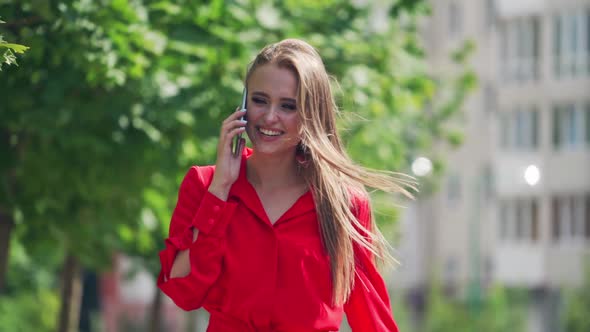 Happy woman talking on the cellphone. Attractive smiling young lady in red dress walking in the city