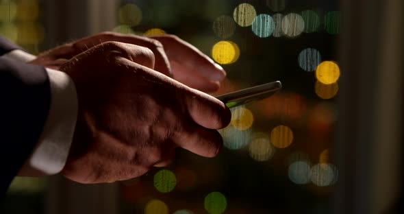 Close-up of Male Hands with a Smartphone on the Background of the Window. He Moves His Fingers