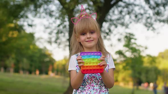 Little Stylish Child Girl Playing Colorful Squishy Silicone Bubbles Sensory Pop It Toy Game in Park