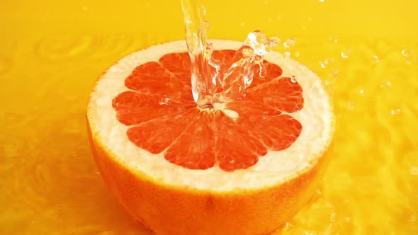 Half of a grapefruit in a jet of water on an orange background. Slow motion.