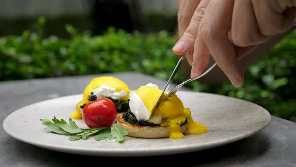 Man Eating Delicious Poached Eggs with Liquid Egg Yolk in Green Outdoor Cafe