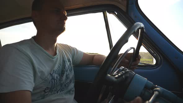 Caucasian Man Holding Hands on Steering Wheel and Driving a Retro Car at Sunset