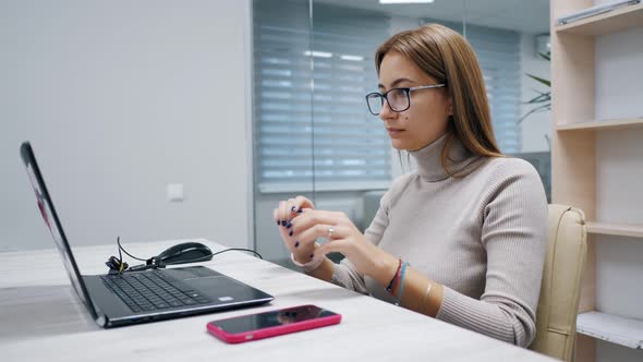 Cute Woman Working at a Laptop and Use Mobile Phone for Break Typing Text in the Office Female