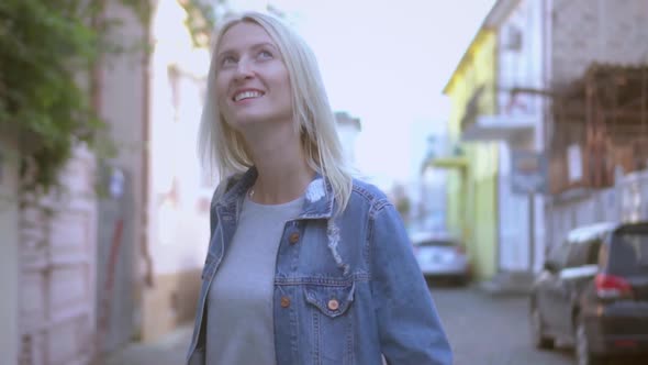 Rear view of young stylish blonde in denim jacket walking through city center