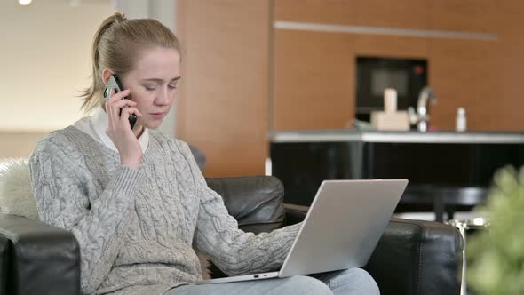 Young Woman with Laptop Talking on Smartphone at Home 