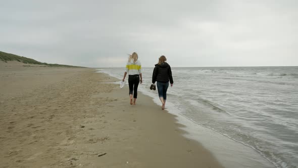 Rear shot of two female girlfriends walking at seashore during holiday trip in Netherlands