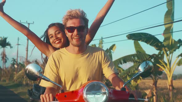 Couple Travelers Riding Scooter at Sunset Woman Raises Hands Up