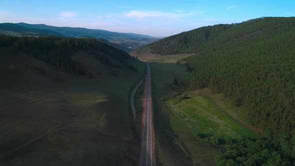 AERIAL, TOP DOWN: Dark Colored Car Driving Down an Asphalt Road Crossing the Vast Forest on a Sunny