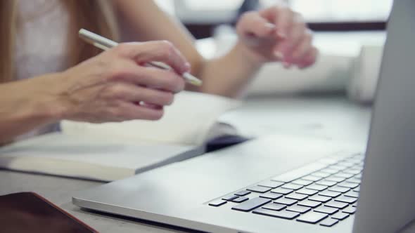 Woman Is Working with Laptop Sitting at Table Checking Information From Notebook