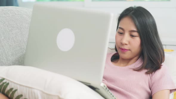 Young business Asian woman working on laptop checking social media while lying on the sofa.