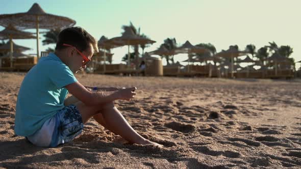 Cute Teenager Playing Mobile Phone at Seashore. Young Man Enjoying Sea at Beach.