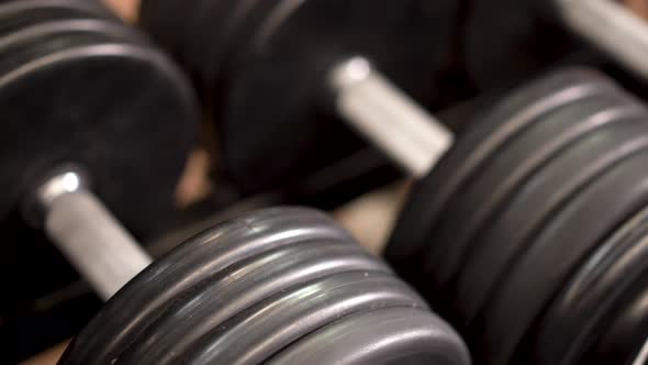 Extreme closeup, slow slider shot to the left looking down on row of dumbbells on a rack.