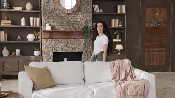 Funny Young Smiling Woman Comedian Having Fun at Home Humorously Hiding Behind Couch Pampering in