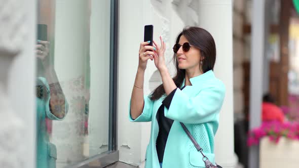 Smiling Beautiful Woman Admiring Taking Photo of Glass Shop Showcase Using Smartphone