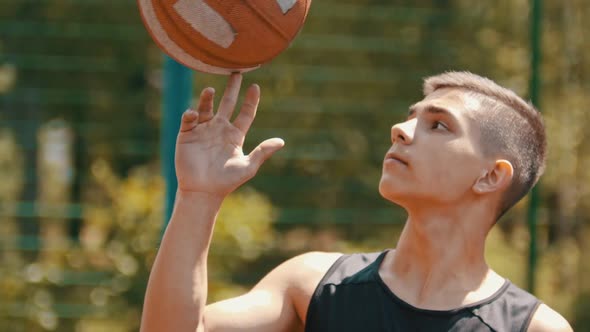 A Teenage Boy Standing on a Sports Ground and Spinning the Basketball Ball on His Finger