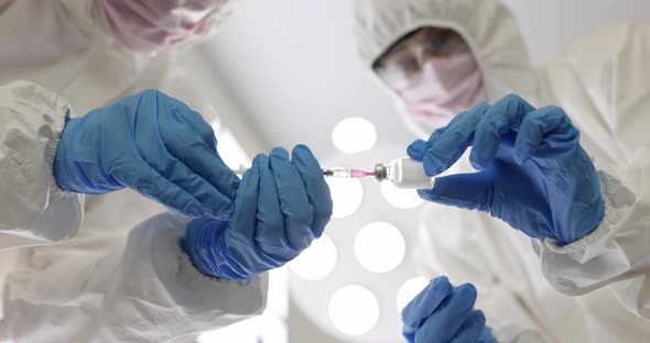 Two Doctors in Gloves and Protective Suits in Masks Draw Syringe with Vaccine or Medicine From Vial