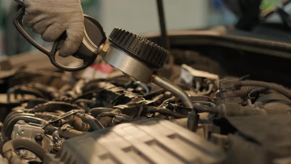 Auto mechanic is changing motor oil into a engine at car station.