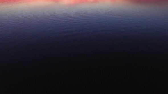 Aerial push in and pan up revealing shot of sunset over a calm lake.