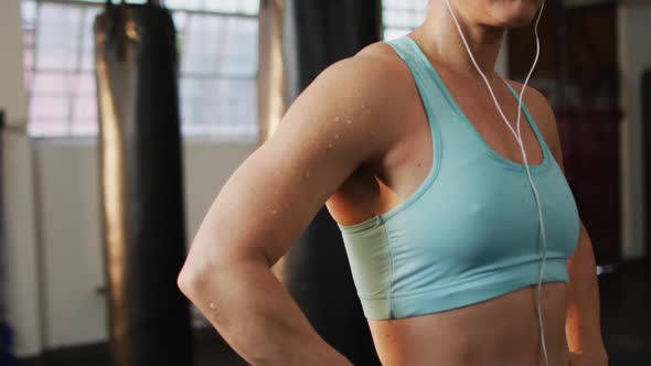 Portrait of fit caucasian woman wearing earphones with hands on hips standing at the gym