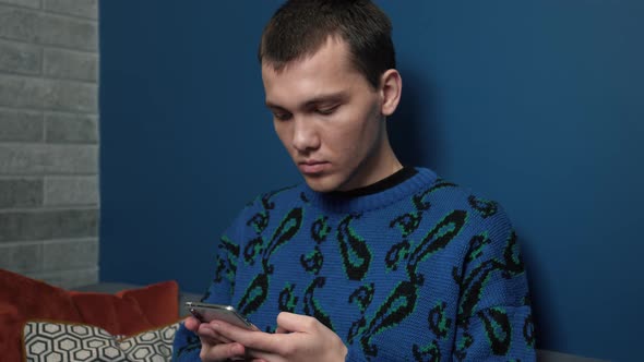 Young Handsome Caucasian Man Uses Smartphone at Home. Man Browses Through Internet, Watches Videos
