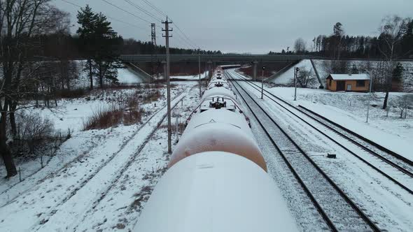 Low Aerial Flight Over Stationary Cistern Tank Train Covered in Snow and Under Bridge During Winter