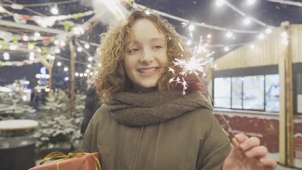 Portrait of happy girl holding sparklers at Christmas fair in European city.