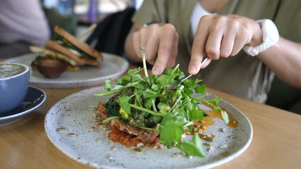 Close Up of Cutting a Vegan Sandwich Topped with Lots of Vegetables and Greens with Cutlery