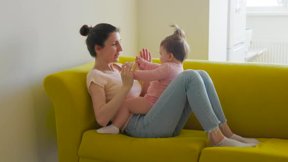 Authentic of Young Mother is Playing with Her Baby Siting on the Yellow Sofa in a Morning