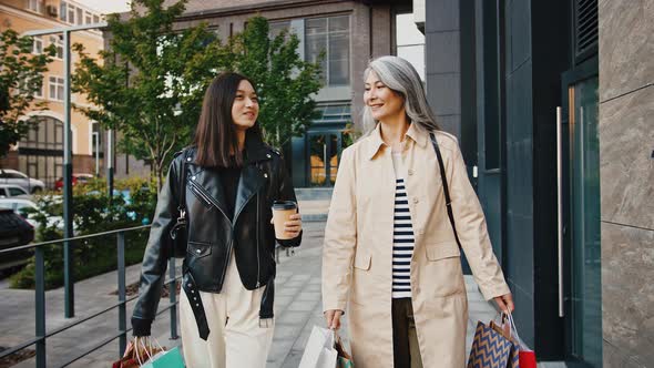 Middleaged Female and Adult Daughter are Smiling Talking Carrying Shopping Packages and Coffee in