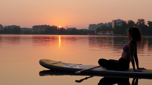 Young Woman on SUP Board He Sits in a Relaxed Position and Looks at the Sunrise