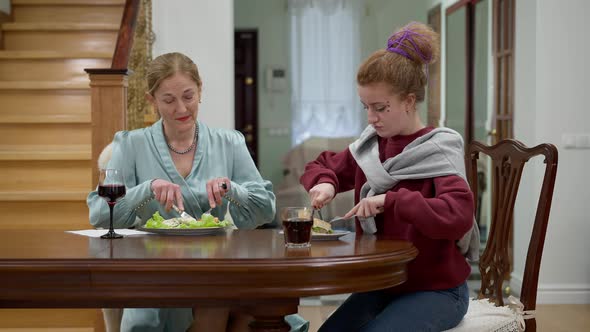 Portrait of Elegant Middle Aged Lady Teaching Hipster Woman Eating with Fork and Knife Indoors