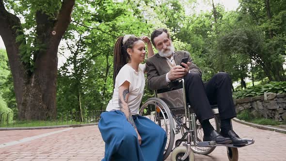 Trendy Girl with Dreadlocks Looking at Smartphone Together with Her Bearded Grandfather