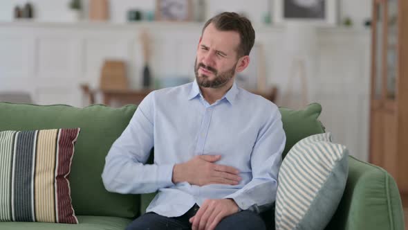 Young Man Having Abdominal Pain While Sitting on Sofa 