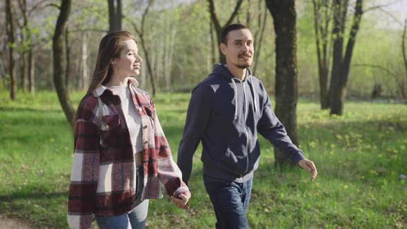 A Pleasant Couple of Young People in Casual Clothes are Walking in the Park in Nature