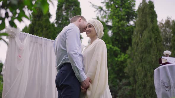 Medium Shot of Loving Caucasian Man Whispering on Ear of Smiling Gorgeous Middle Eastern Woman in