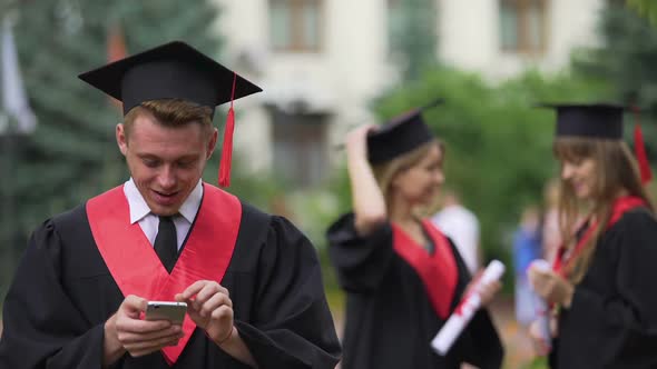 Cheerful Graduate Reading Good News on Smartphone and Smiling, Graduation