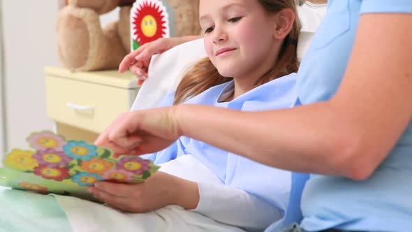 Smiling woman giving a teddy bear to a smiling girl in a bed