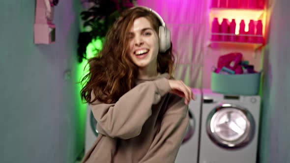 Nice Young Woman with Curly Brown Hair in Beige Headphones and Beige Sports Suit Dances Against