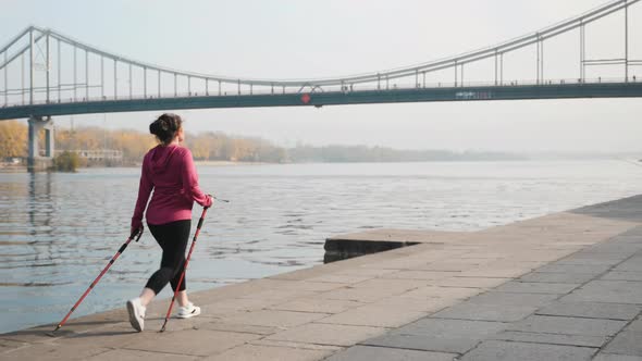 Nordic Walking, Fit chubby woman with nordic poles walking alone city river quay and bridge training