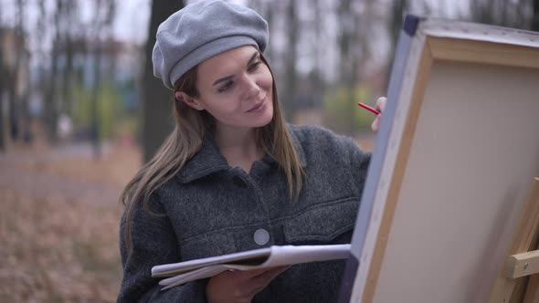 Joyful Talented Woman Painting on Canvas Putting Brush in Mouth Grimacing Looking at Camera