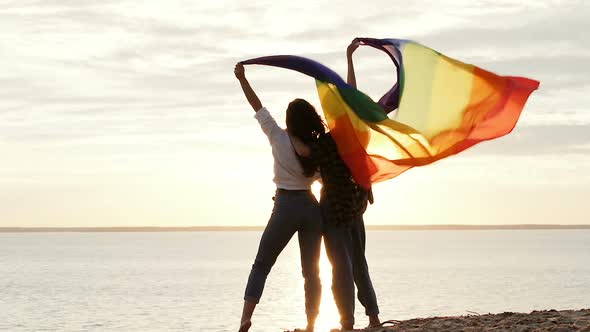 Couple of woman holding big rainbow flag.