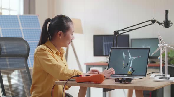 Asian Woman Looking At A Laptop Showing Wind Turbine On The Table That Next To The Solar Cell