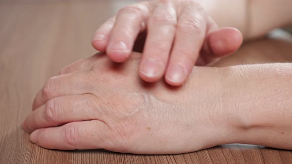 Elderly Woman Strokes Own Wrinkled Hand Lying on Table